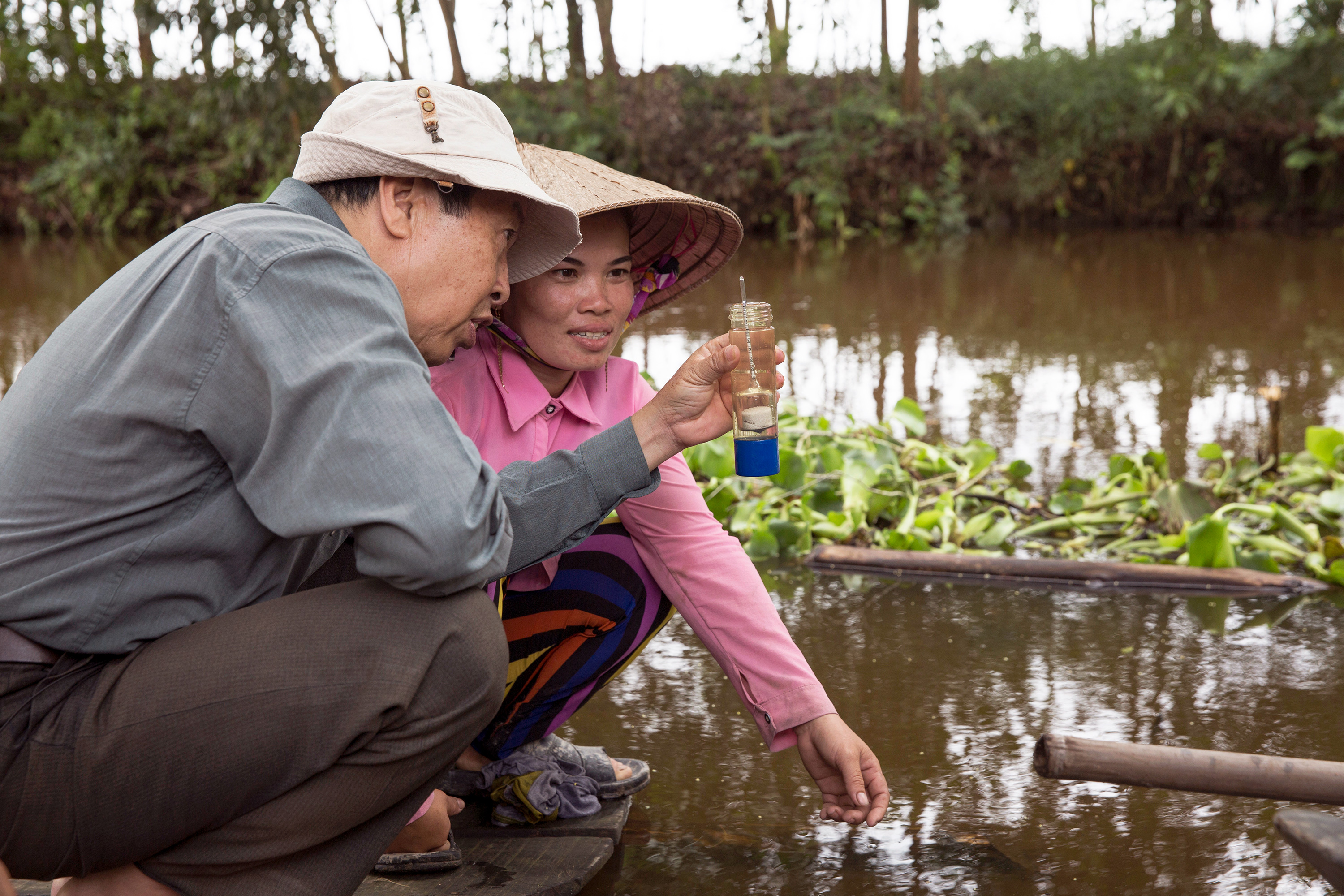 Two people in a rice field look at a water sample